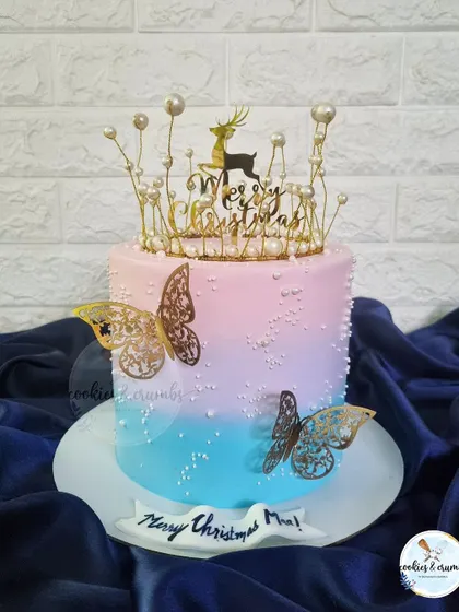 A beautiful Christmas cake with a pink and blue ombre effect. The design is elevated with a delicate pearl crown and golden butterflies, making it feel magical.