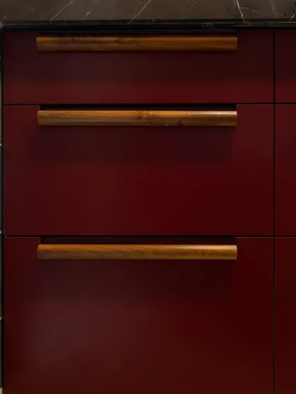 The texture and warmth of the wooden handles are a key feature in this kitchen. They are not just functional but are a design element in themselves, adding a layer of craftsmanship and softening the bold red of the cabinetry.