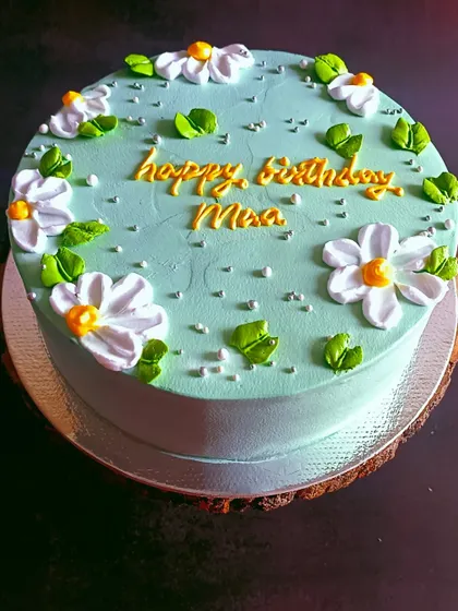 A simple and pretty mixed fruit cake with a pastel green frosting and delicate daisy decorations.