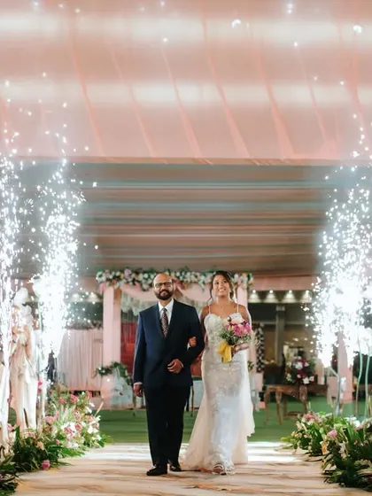 A father proudly walks his daughter down the aisle, illuminated by sparklers, during a beautiful Christian wedding ceremony.
