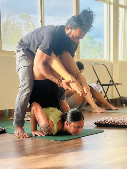 An instructor providing a deep adjustment in an advanced inversion. This level of guided assistance helps a student safely explore the limits of their flexibility and strength.