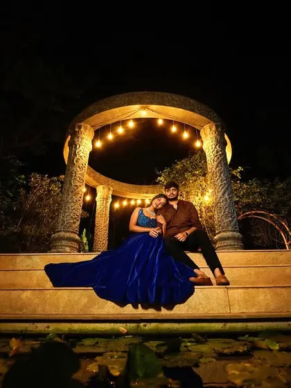 A dramatic wide shot of a couple sitting on steps under a beautifully lit gazebo at night.