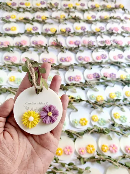 A hand holding one of the delicate floral wax sachets, showing the handmade quality and design.
