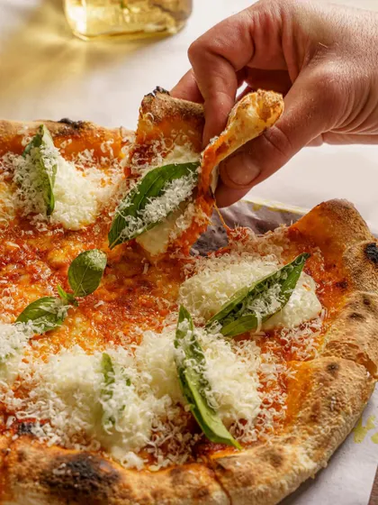 A classic Margherita pizza, with a slice being lifted. This shot highlights the fresh ingredients and the perfect crust, a staple for any pizzeria's marketing.