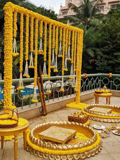 A beautiful poolside Haldi ceremony setup. The decor features a frame draped with yellow marigold garlands and traditional brass urlis for the ceremony, combining tradition with a resort-like feel.