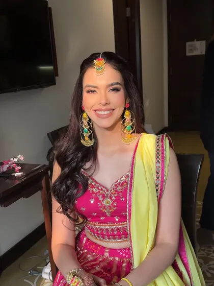 Bright and beautiful for Mehendi. This look features soft shimmer eyes with a pop of pink, paired with an effortlessly natural base and soft nude lips to complement her colorful outfit.