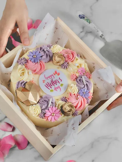 A beautiful Mother's Day cake decorated with a wreath of buttercream flowers, presented in a lovely wooden box.