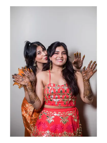 The bride and her sister share a fun, loving moment, showing off their beautiful mehendi designs. Capturing family bonds is a key part of our work.