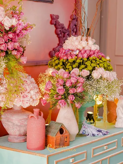 A collection of floral arrangements and decorative objects on a mint-green console table. The mix of colors and textures creates a visually rich and charming display.