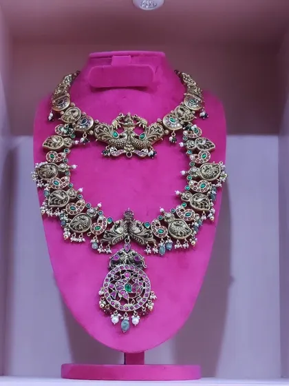 A close-up of a beautiful antique finish haram with intricate carvings and a ruby and emerald pendant.