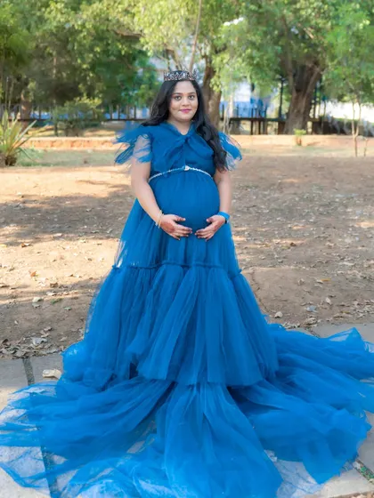 A regal outdoor portrait of a mom-to-be wearing a crown with her royal blue gown. The dress spreads out beautifully on the ground around her.
