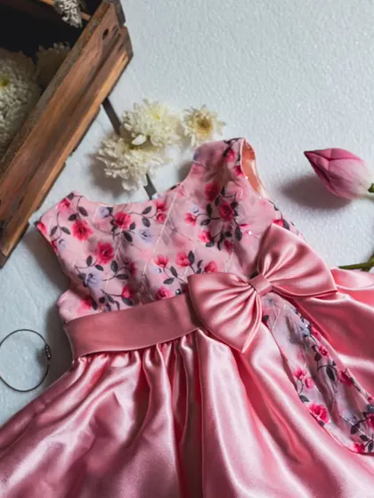 This bright peach dress is crafted from luxurious leather satin for a beautiful sheen. The design is elevated with an embroidered floral bodice and a large, elegant bow that adds a touch of glamour.