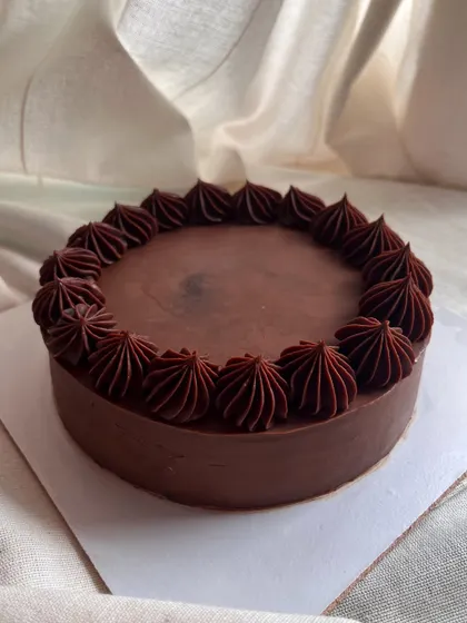 A classic 6-inch eggless chocolate cake. It's a rich chocolate sponge covered entirely in smooth, dark chocolate ganache with a simple piped border.