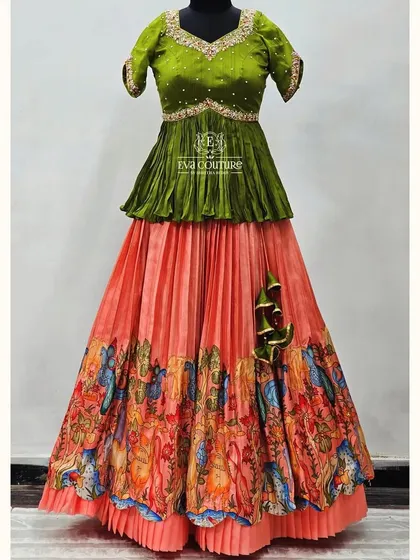 A stunning gown-style lehenga with a hand-painted skirt. The olive green peplum top is paired with a peach skirt that has a beautiful, artistic border depicting a traditional scene.