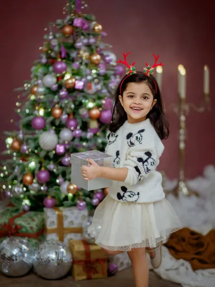All smiles and holiday cheer. This little girl, with her reindeer antlers and festive sweater, is ready to celebrate Christmas in our specially designed studio setup.