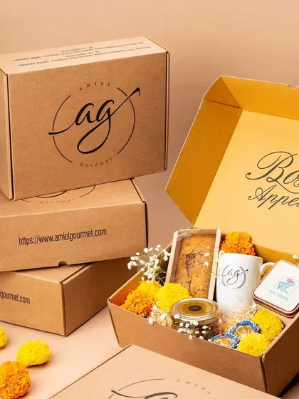 A beautifully arranged Diwali hamper, ready for gifting. This box is filled with festive treats, including a tea cake, cookies in a jar, an AG mug, and decorated with marigold flowers.