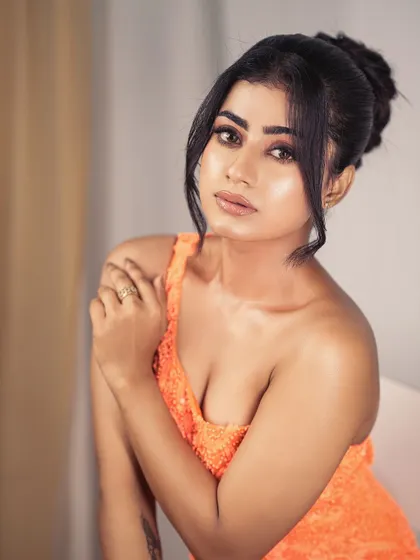 A beauty shot focusing on the neckline of the orange gown. The one-shoulder design is modern and provides a perfect frame for glamorous makeup.