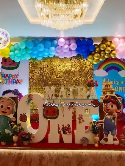This grand Cocomelon first birthday setup features a gold sequin wall and a huge balloon arch. The large light-up 'ONE' prop makes for a perfect centerpiece on the stage.