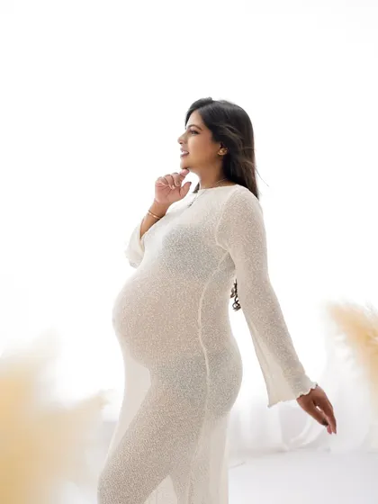 A candid and happy portrait. The mom-to-be is captured in a moment of joy, her sheer white dress glowing in the soft light.