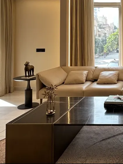 Sunlight streams into the living room, highlighting the textures of the plush leather sofa and the dark marble coffee table. We prioritize natural light in our designs to create bright and uplifting living environments.
