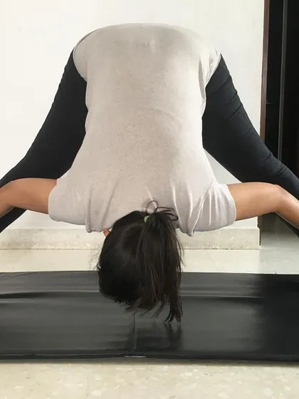 This student is in the fourth variation of Prasaritha Padottanasana, holding the ankles to deepen the forward bend and inversion.