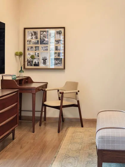 A classic wooden desk and chair create a simple yet elegant workspace within a bedroom, personalized with a photo collage.