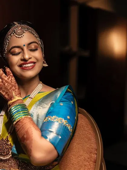 A happy, smiling bride putting on her earrings. The makeup highlights her glowing skin and bright eyes, creating a look of pure joy.