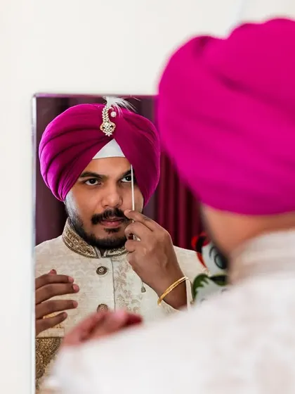 The final touches. The groom adjusts his turban ornament, or 'sarpech', in the mirror, a key part of the Sikh groom's getting-ready process.