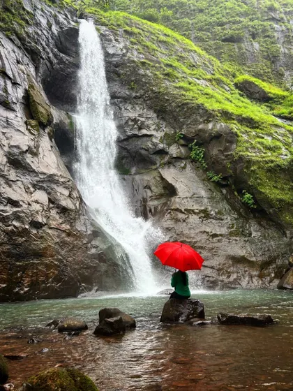 A teaser for our Maharashtra monsoon trek, showing a trekker with a red umbrella at a serene waterfall.
