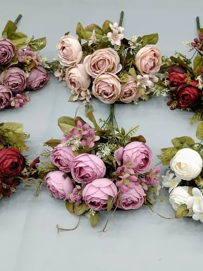 A selection of artificial ranunculus and rose bunches in various vintage-inspired colors like mauve, dusty rose, and deep red.