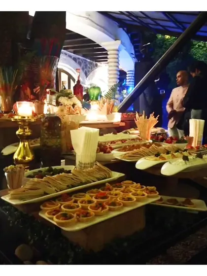 An evening buffet setup at the Garden of Five Senses, with ambient lighting highlighting the array of tarts, sandwiches, and other delicacies.