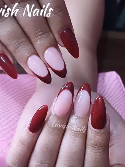 A modern twist on the French manicure, featuring a deep, glossy red tip on a long, almond-shaped nail.