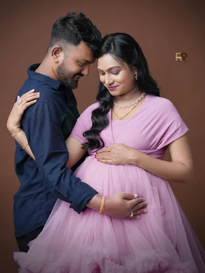 A tender moment shared between the couple. This close-up shot focuses on their connection as they both gently hold the baby bump, dressed in a lovely pink gown.