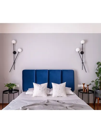 This bedroom features a symmetrical design with a deep blue headboard and modern globe sconces. The simplicity of the arrangement creates a calm and balanced feeling.