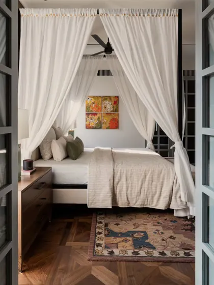 The master bedroom in the Pràna house, seen through open doors. The four-poster bed draped in sheer white fabric creates a romantic, dream-like focal point.