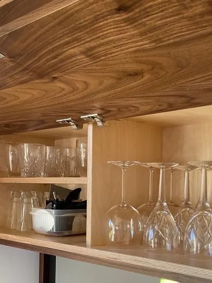 The overhead unit features a lift-up door with soft-close hinges, revealing ample storage for various types of glassware. The internal shelving is made from light-coloured birch plywood, which contrasts nicely with the dark walnut exterior.
