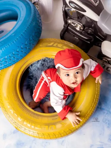 A few action shots from an F1 and racing-inspired photoshoot. The baby is styled in a red racing uniform, captured with fun expressions among tires and toy vehicles.