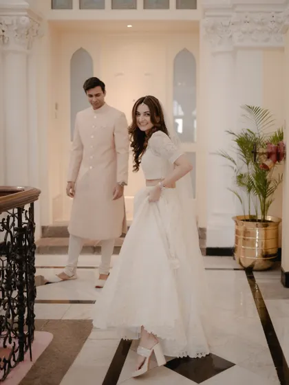 A playful moment in the grand corridors of the Taj. The bride lifts her lehenga, sharing a smile with her groom in their elegant white wedding attire.