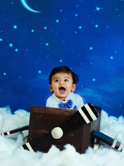 A toddler's imagination takes flight in this airplane-themed studio setup. The little boy looks up with excitement from a propeller plane prop set against a starry night sky.