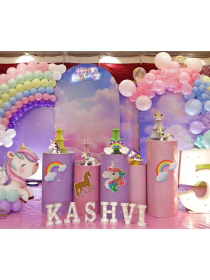 A magical unicorn-themed 5th birthday party featuring a rainbow balloon arch, a dreamy cloud backdrop, and a large light-up number '5'.
