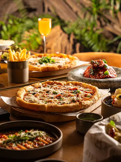 A table laden with pizzas, pastas, and appetizers in a warm, rustic setting. This image showcases a hearty, communal dining experience.