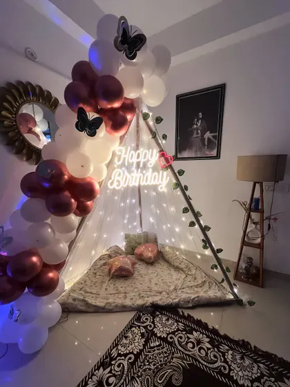 A cozy and bohemian-style birthday surprise at home. This setup features a small tent decorated with fairy lights and a balloon garland, creating a perfect little retreat.