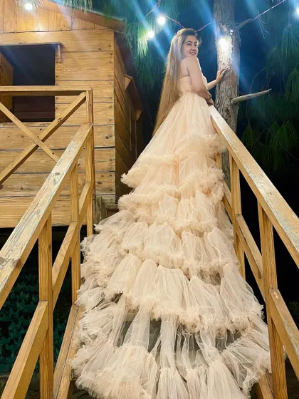 Sometimes you just need to make your own magic. A model poses on a wooden staircase in a treehouse, her nude-colored ruffled trail gown cascading down the steps.