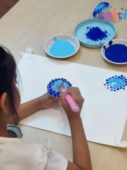 A girl carefully dabs paint onto her bubble wrap stamp. This activity requires focus and helps develop her fine motor skills.