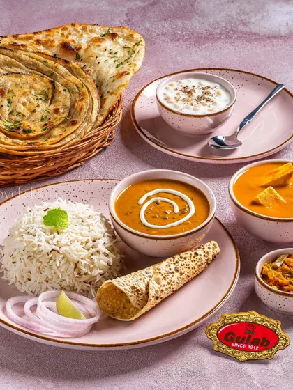 A classic North Indian thali with dal makhani, shahi paneer, rice, and lachha paratha, presented on elegant pink dinnerware.
