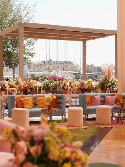 An outdoor lounge with a stunning view, featuring pastel blue sofas, colorful cushions, and an abundance of floral arrangements under a wooden pergola.