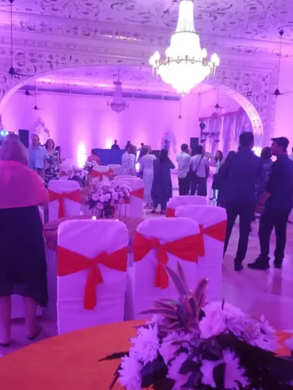 An indoor sangeet or reception setup with beautiful purple uplighting. The elegant chandeliers and floral centerpieces create a sophisticated party atmosphere for guests to enjoy.