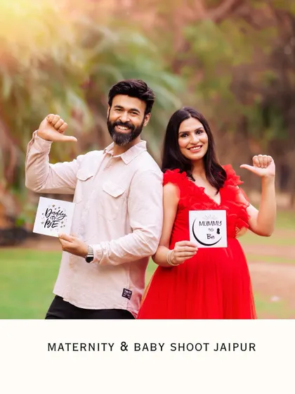 A fun outdoor announcement photo. The couple stands back-to-back, holding signs that say "Daddy to be" and "Mummy to be," sharing their exciting news with a smile.
