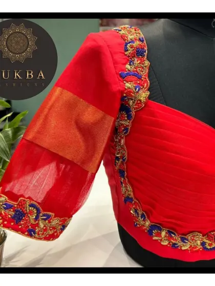 A modern take on a classic red blouse, this design features a sheer organza panel on the sleeve, framed by delicate floral embroidery. It adds a touch of lightness to the overall look.