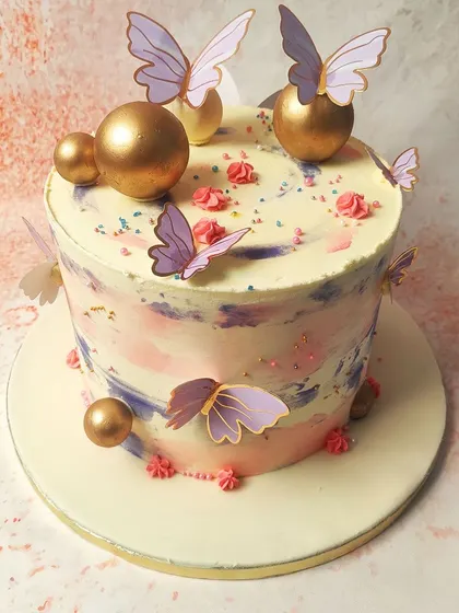 We paint with pastels on this abstract butterfly cake. A watercolor-like blend of pink, purple, and blue buttercream creates a dreamy canvas for delicate purple and gold butterflies and shimmering gold spheres, resulting in a piece of edible art.